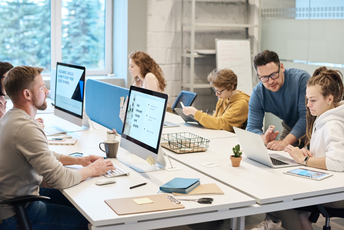 A group of people sitting around a table with computers Description automatically generated with medium confidence